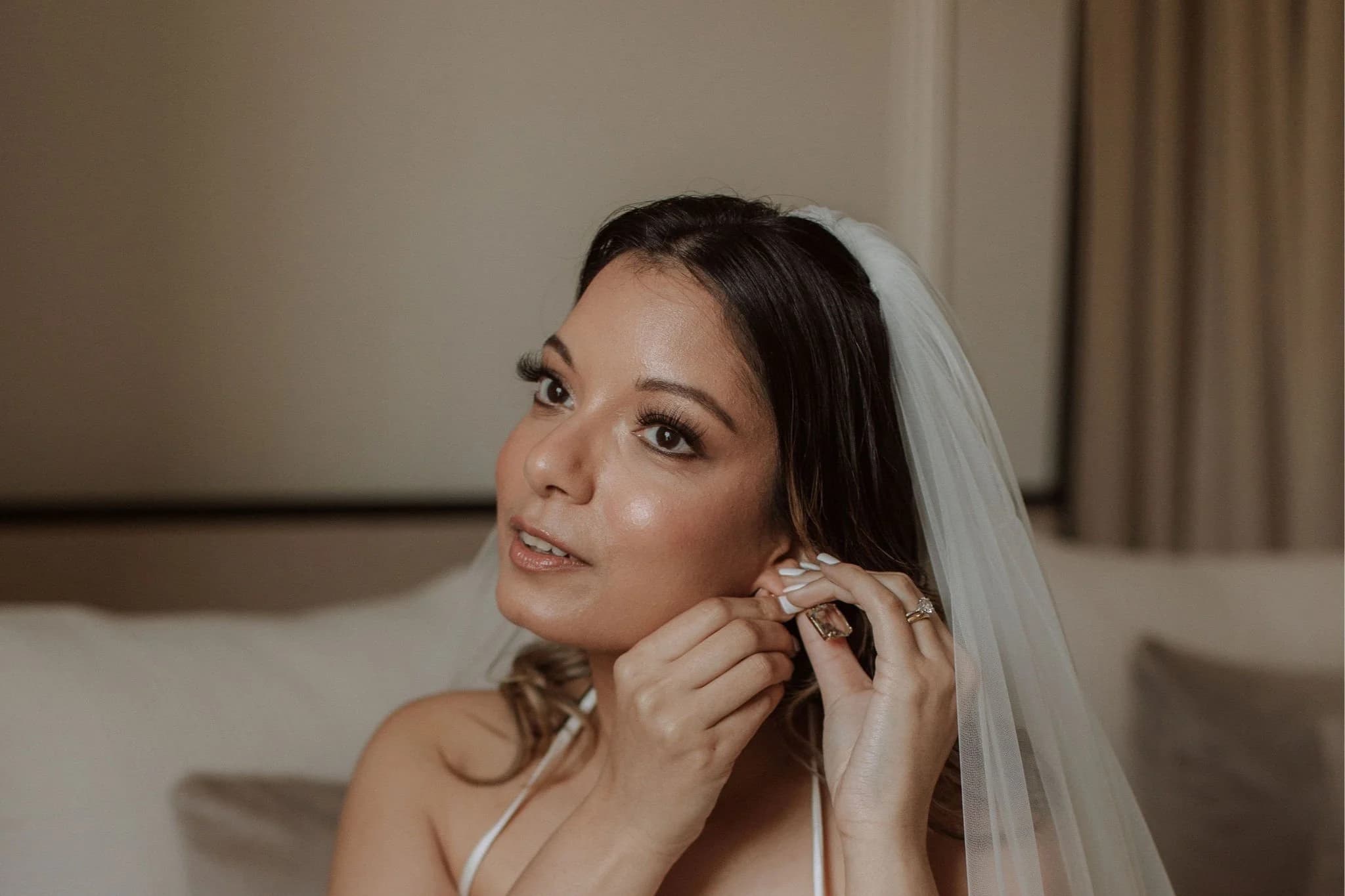 Bride in a veil putting on an earring, soft glam makeup