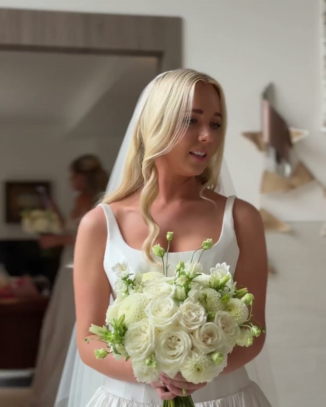A bride in her veil walking in to see her bridesmaids, holding white roses