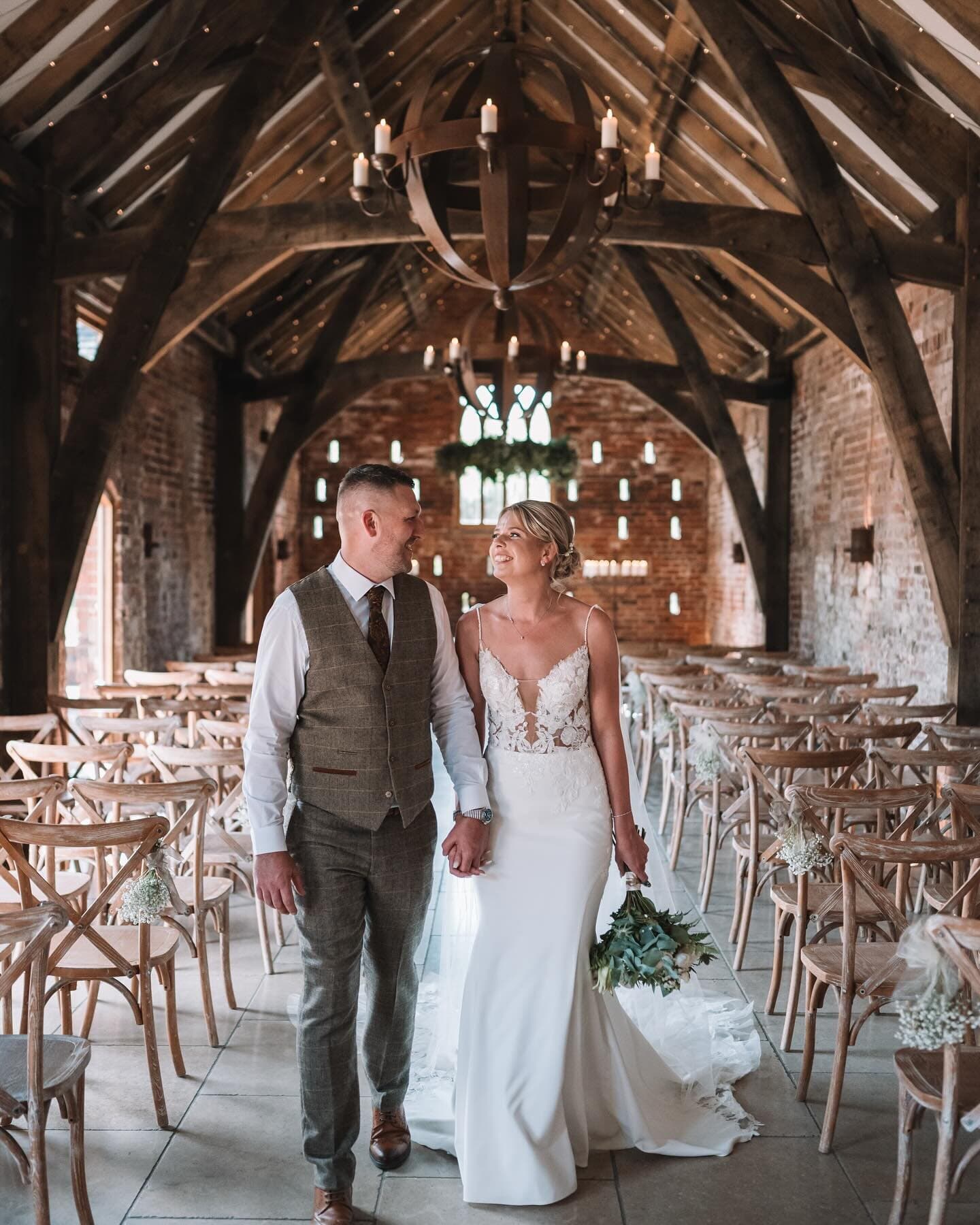 Sian and her husband walking back up the aisle of a timbered barn
