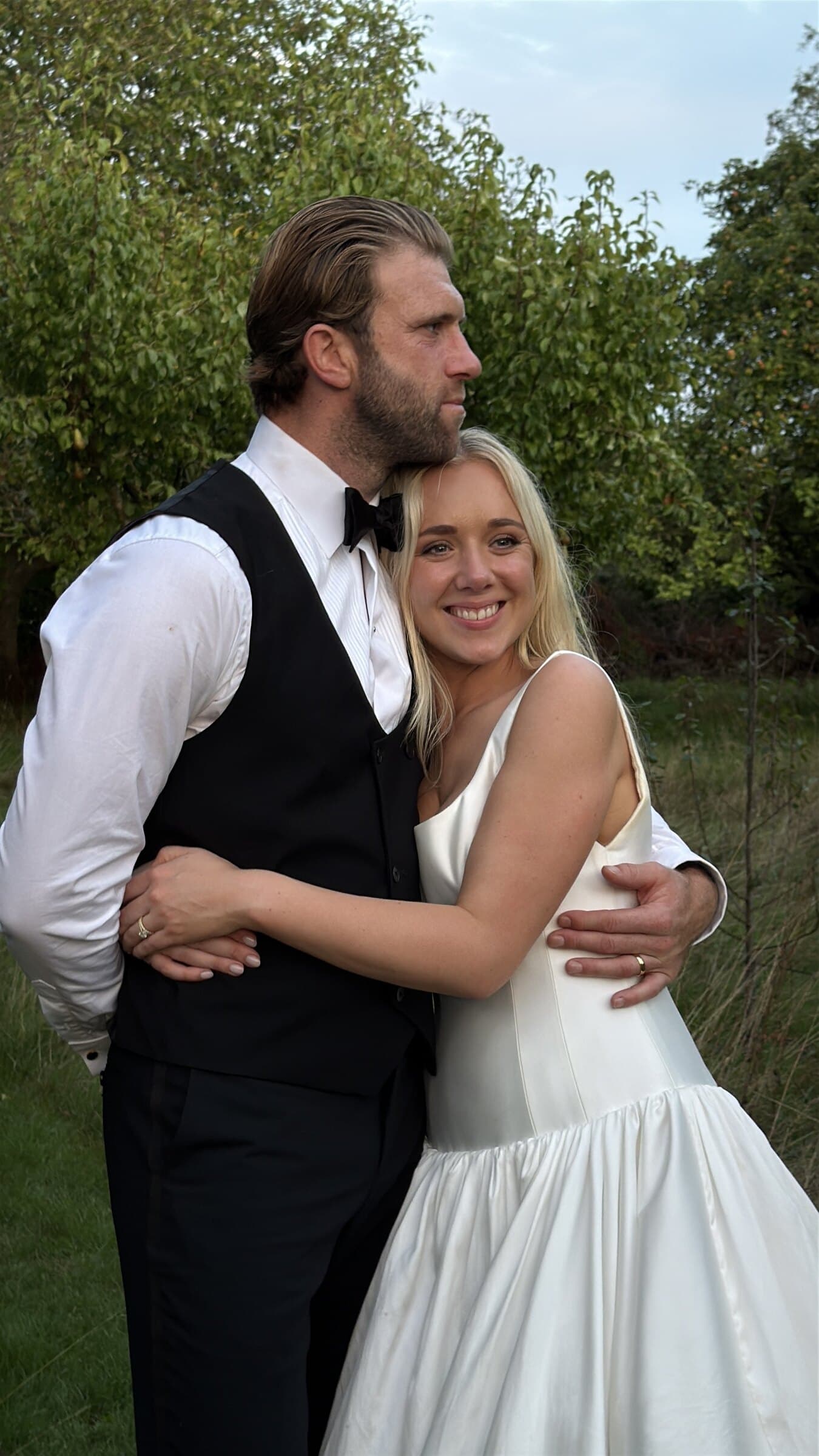 A bride and groom holding each other in a garden at the end of the day